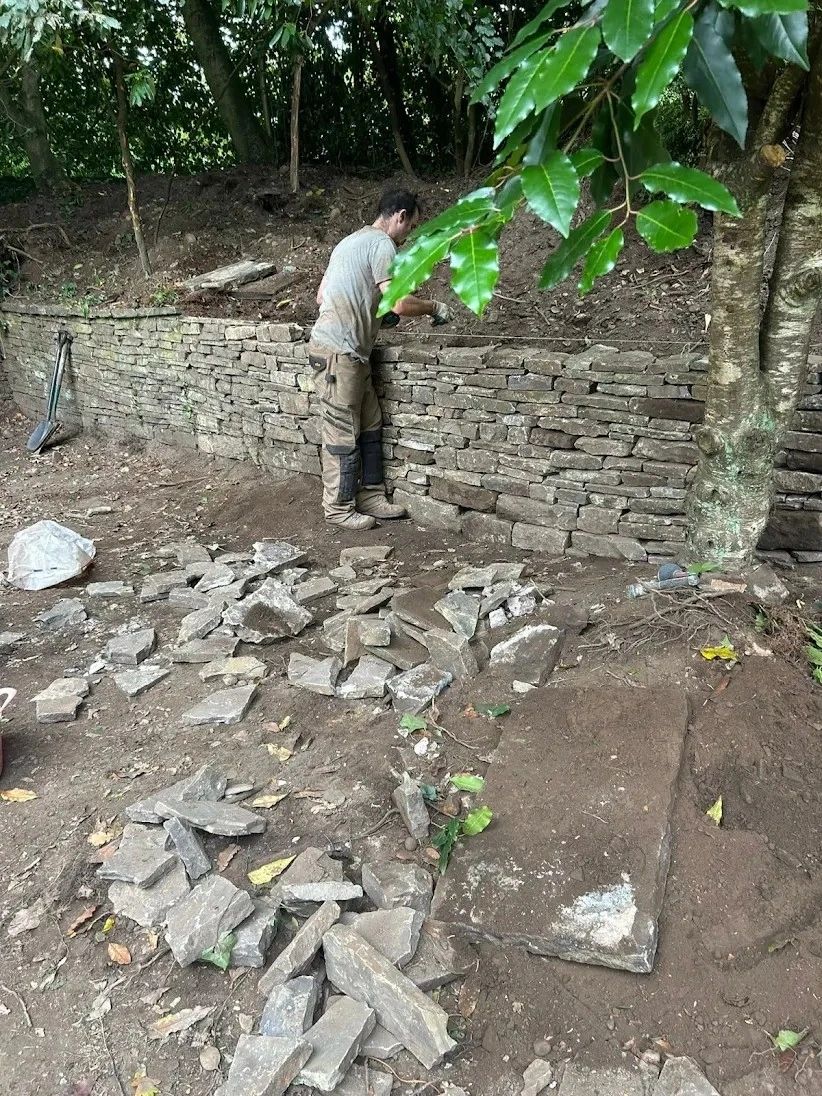 A person building a stone wall outdoors surrounded by nature.