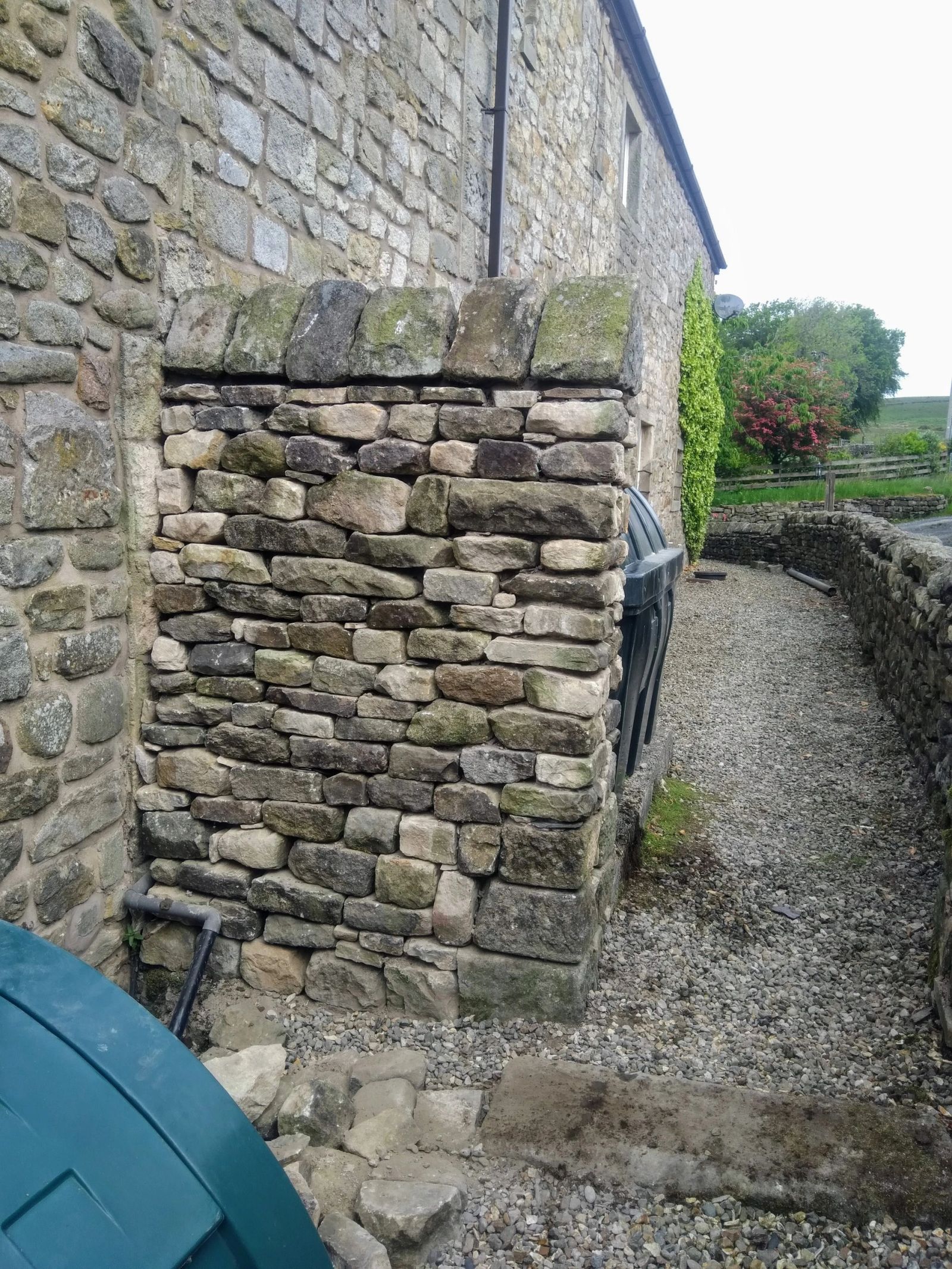Rebuilt stone pier with new coping stones beside a stone barn.